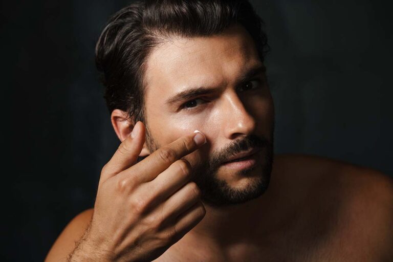 young half naked man looking at camera while applying face cream